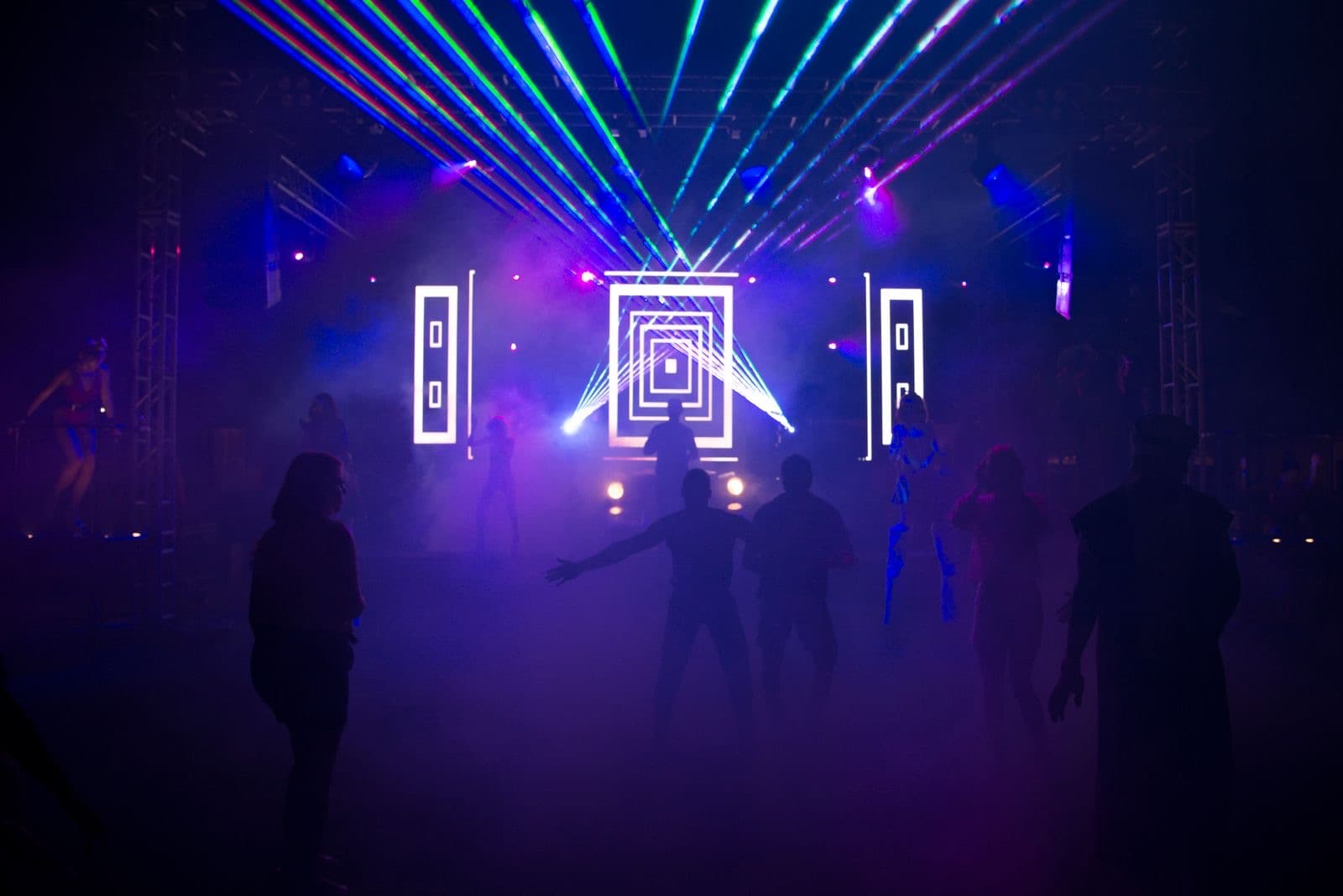 Silhouetted crowd dancing under colored lasers and smoke