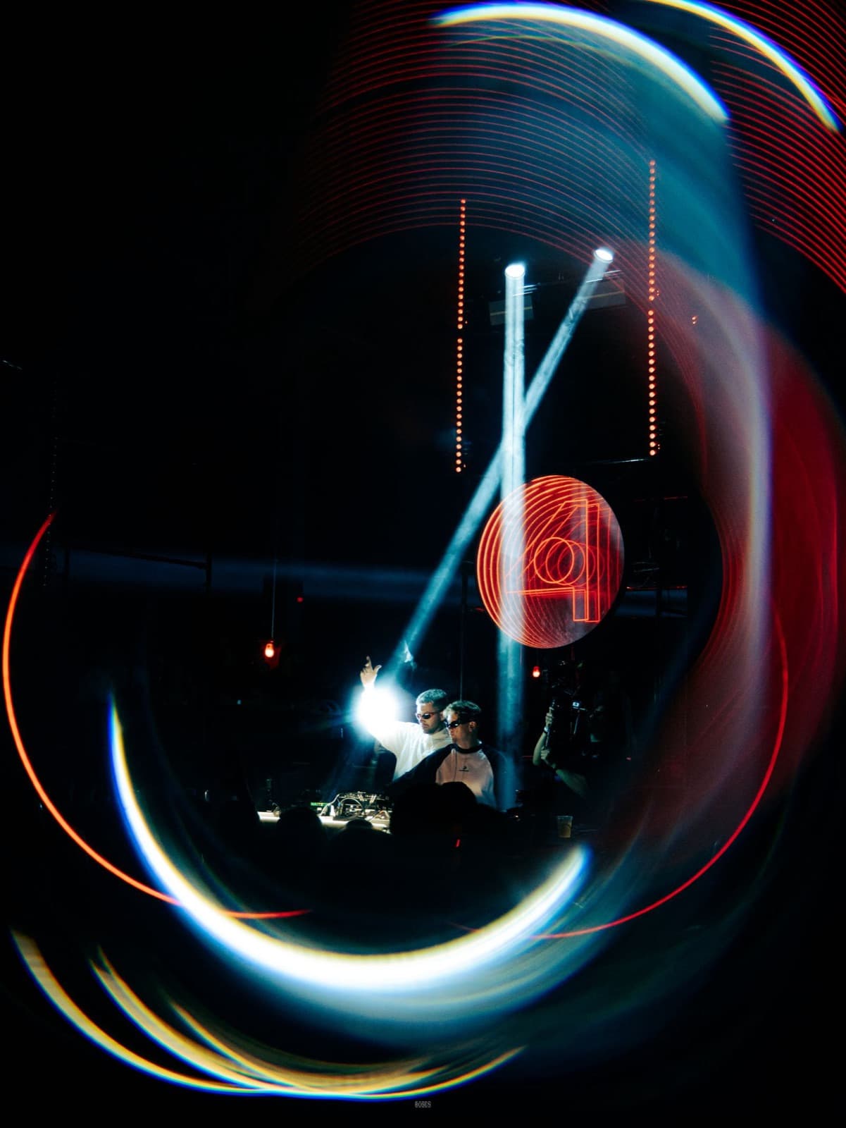 DJ behind the decks, lit by beams and haze in a club